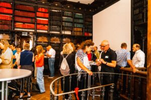 ca. 20 Personen stehen in alter Bibliothek und unterhalten sich